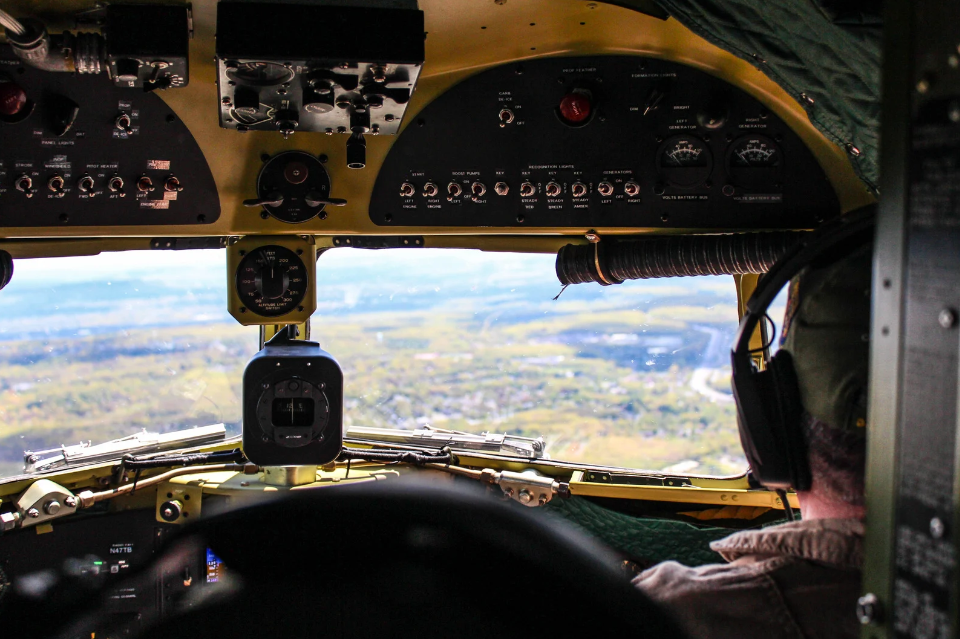 Image of an airplane cockpit. The airplane is flying and the setting outside is vibrant green grass.