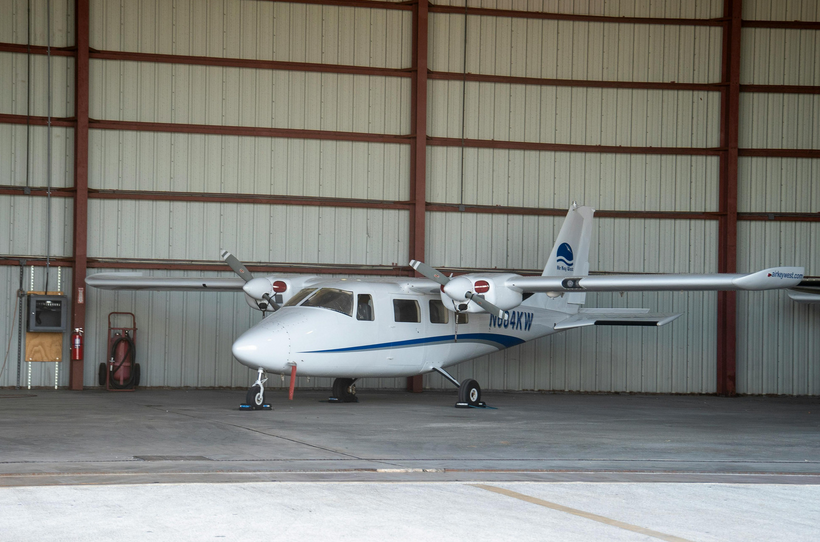 An image of an airplane in a hangar. The airplane is small and white, and has two propellers.