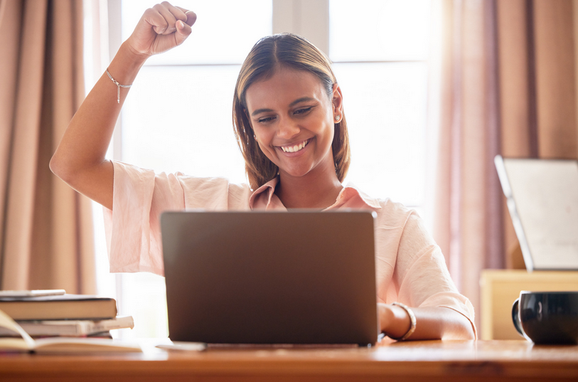 Image of a young woman working on her laptop. She is happy and her fist is raised into the air.